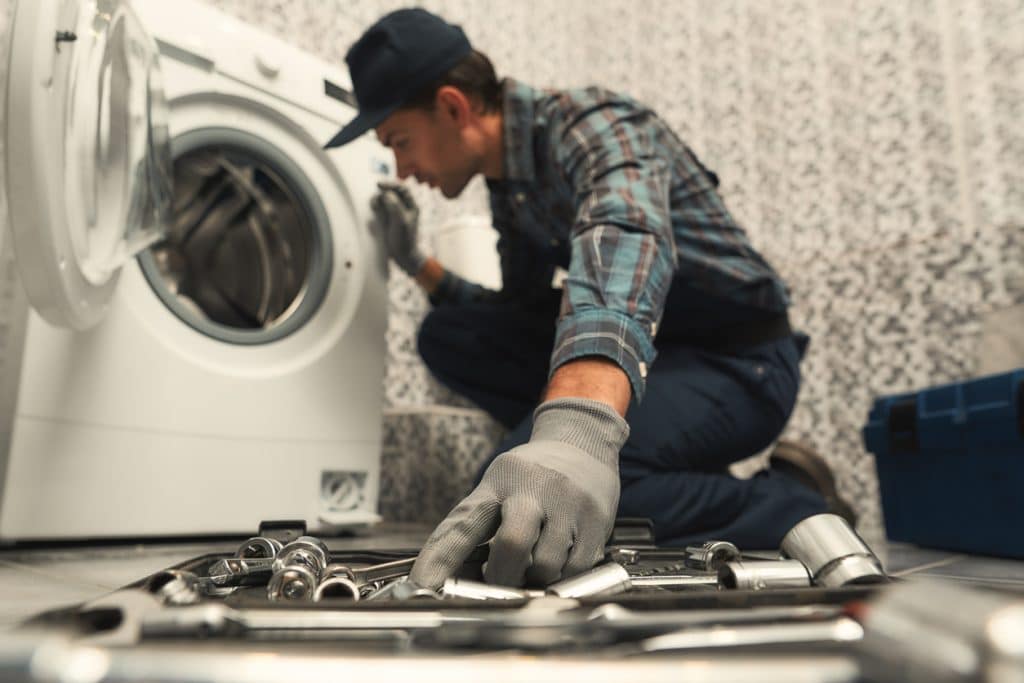 handyman sitting next to broken washing machine